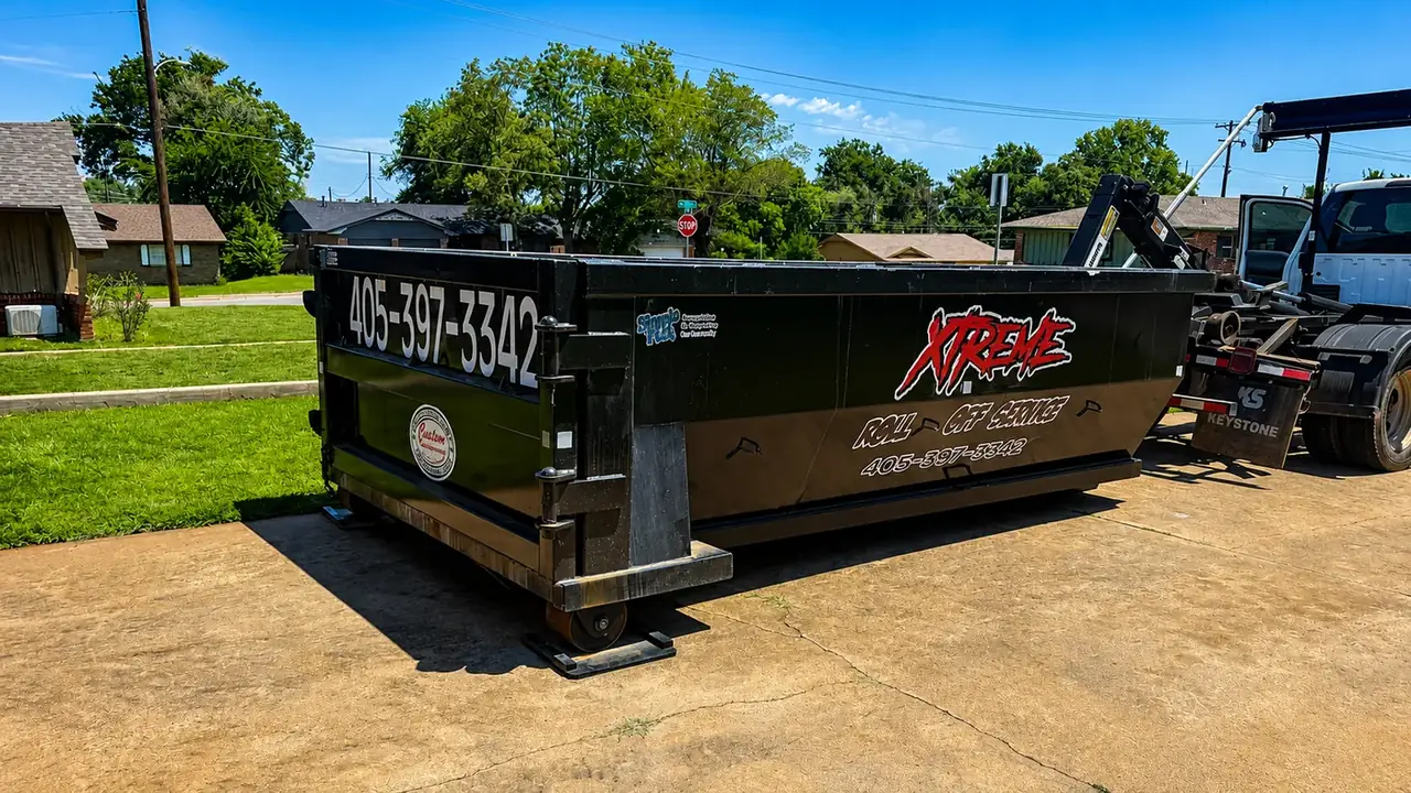 White Xtreme Roll Off Service truck lifting a black dumpster in a residential setting